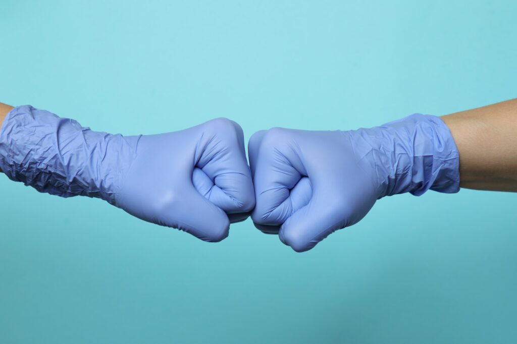 Hands in medical gloves greeting with fist bump on blue background